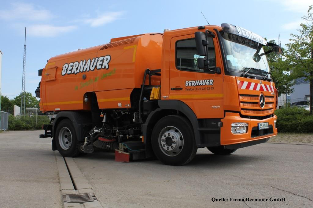 Oranger Kehrmaschinen-Lkw mit Aufschrift "BERNAUER" und Straßenkehrbürsten unter dem Aufbau.