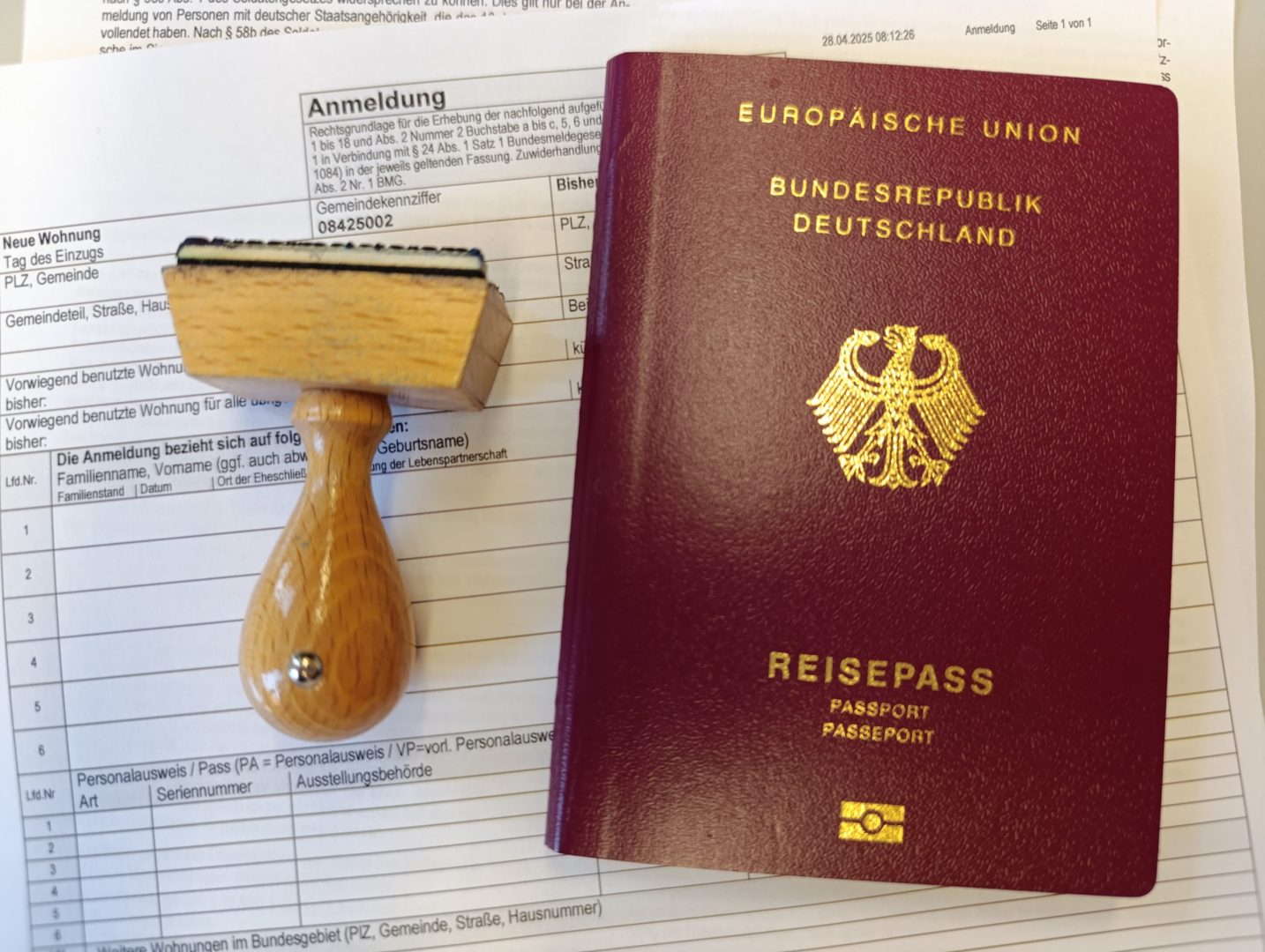 Deutscher Reisepass und Holzstempel auf ausgefülltem Anmeldeformular.