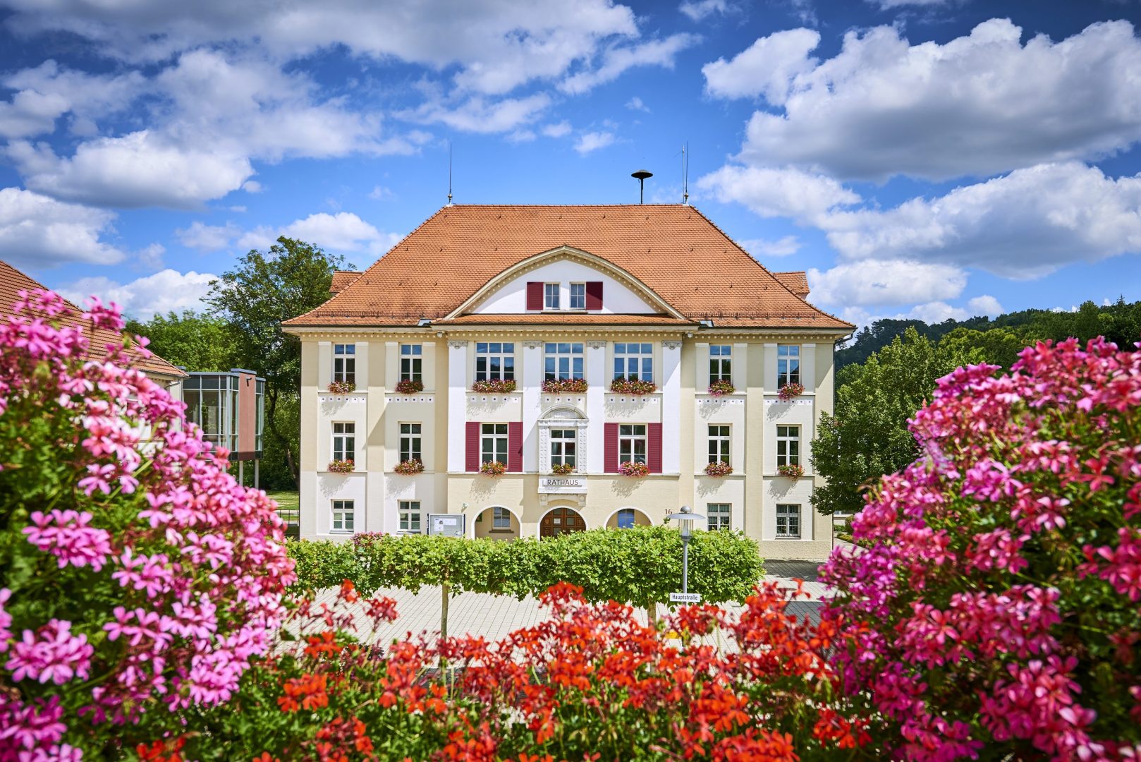 Barockes Rathausgebäude mit rotem Ziegeldach, Fensterblumen und bunten Blumen im Vordergrund